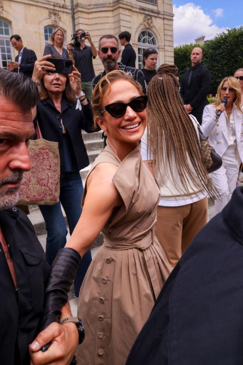 Jennifer Lopez wearing a brown dress and black sunglasses smiles to people in Paris