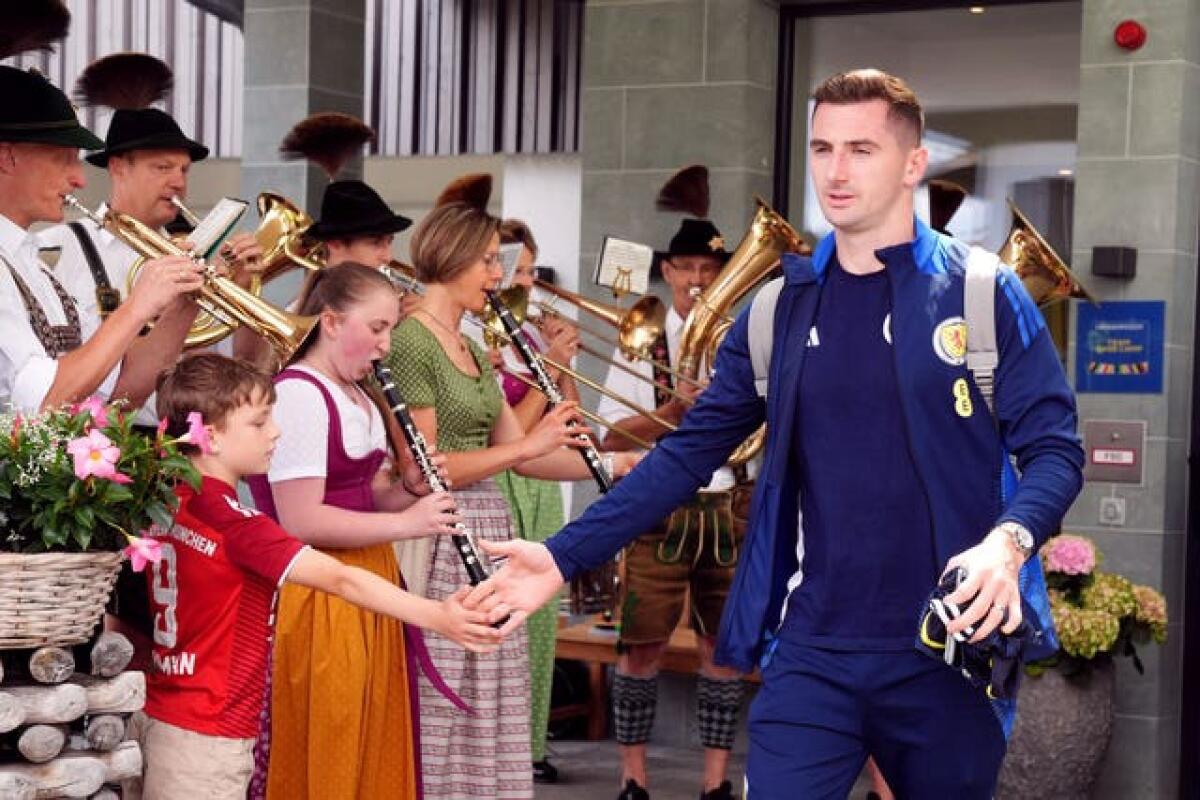 Kenny McLean greets a young football fan as he leaves Scotland's hotel while a Bavarian band play their instruments in the background